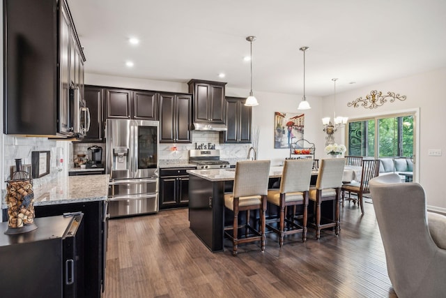 kitchen with pendant lighting, stainless steel appliances, light stone countertops, and a kitchen island with sink