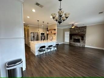 kitchen featuring pendant lighting, a fireplace, ornamental molding, a kitchen bar, and dark hardwood / wood-style flooring