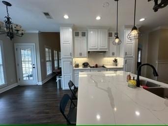 kitchen featuring light stone counters, sink, hanging light fixtures, and white cabinets