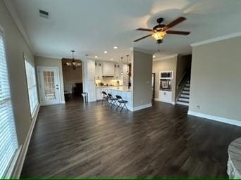 unfurnished living room featuring dark hardwood / wood-style flooring, crown molding, and ceiling fan with notable chandelier