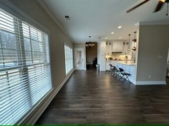 unfurnished living room featuring ceiling fan with notable chandelier, ornamental molding, and dark hardwood / wood-style floors