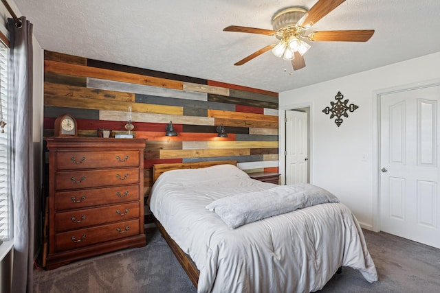 bedroom with ceiling fan, dark carpet, wooden walls, and a textured ceiling