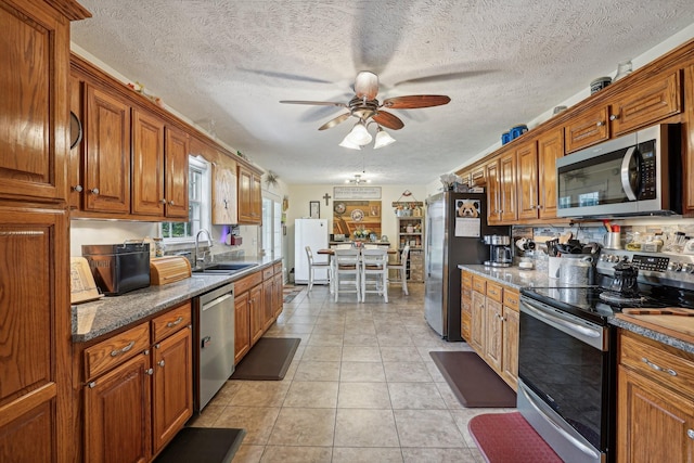 kitchen with appliances with stainless steel finishes, sink, dark stone countertops, light tile patterned floors, and ceiling fan