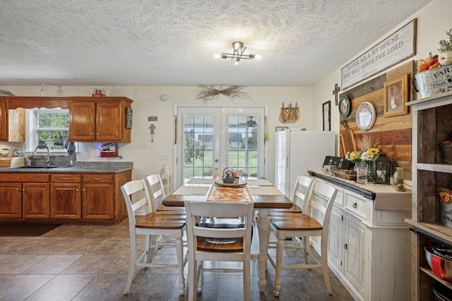 dining area with sink, a chandelier, a textured ceiling, and french doors