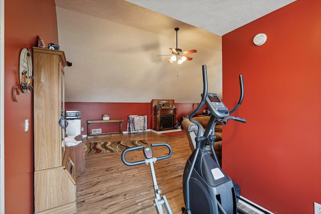 exercise room with ceiling fan, lofted ceiling, light hardwood / wood-style floors, and a textured ceiling