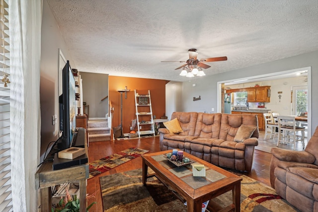 living room featuring ceiling fan, light hardwood / wood-style flooring, and a textured ceiling