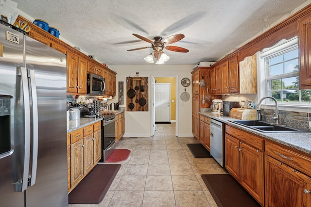 kitchen featuring sink, stainless steel appliances, light stone countertops, a textured ceiling, and light tile patterned flooring