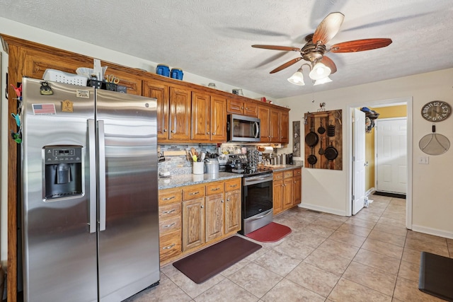 kitchen with ceiling fan, stainless steel appliances, light stone counters, a textured ceiling, and light tile patterned flooring