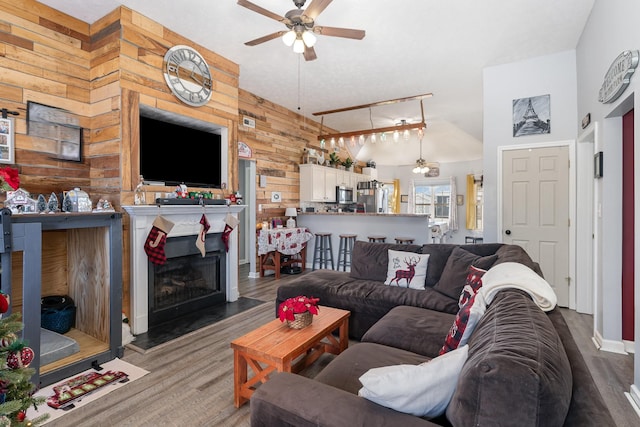 living room featuring ceiling fan, wood-type flooring, wooden walls, and lofted ceiling