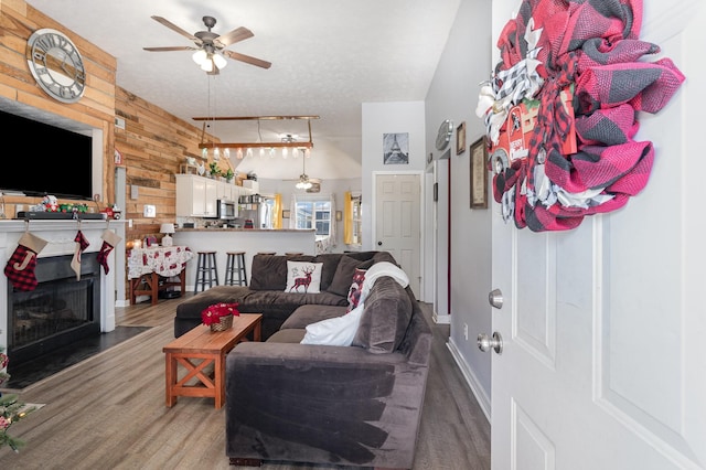 living room featuring wood-type flooring, a textured ceiling, ceiling fan, and wooden walls