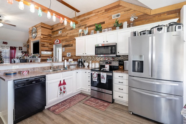 kitchen with sink, appliances with stainless steel finishes, white cabinetry, hanging light fixtures, and wood walls