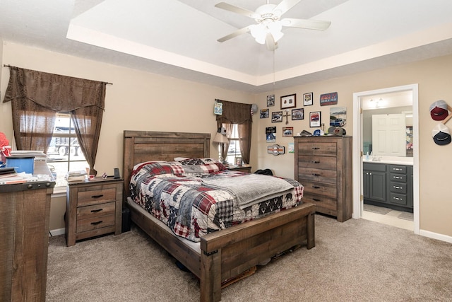 bedroom featuring light carpet, a tray ceiling, ceiling fan, and ensuite bathroom