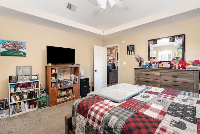 carpeted bedroom with a raised ceiling and ceiling fan