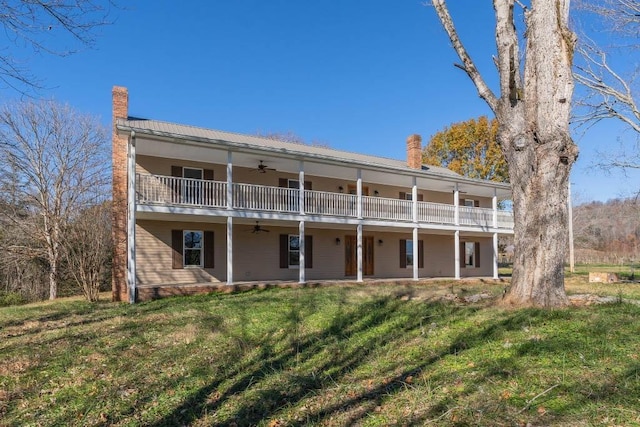 back of property featuring ceiling fan, a balcony, and a lawn