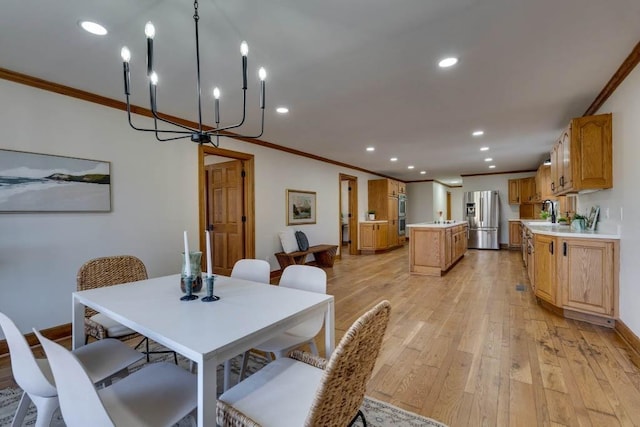 dining space featuring crown molding, sink, an inviting chandelier, and light wood-type flooring