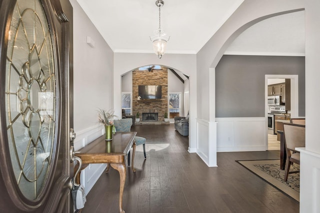 foyer entrance with an inviting chandelier, a stone fireplace, ornamental molding, and dark hardwood / wood-style floors