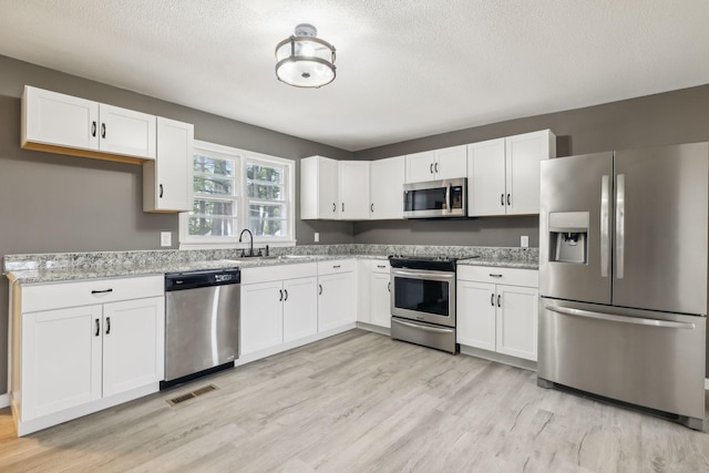 kitchen featuring light stone counters, light wood-type flooring, white cabinets, and appliances with stainless steel finishes