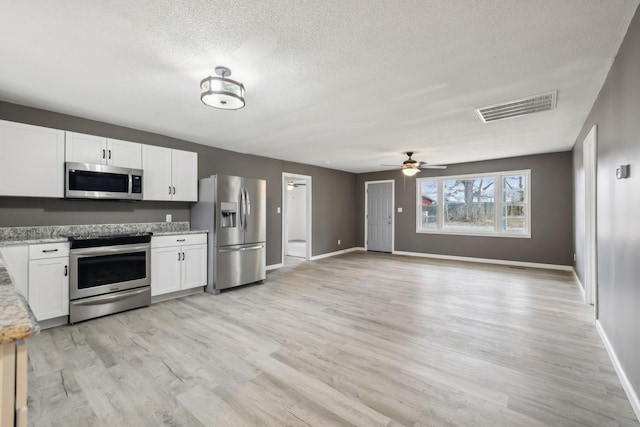 kitchen with white cabinetry, light wood-type flooring, stainless steel appliances, light stone countertops, and a textured ceiling