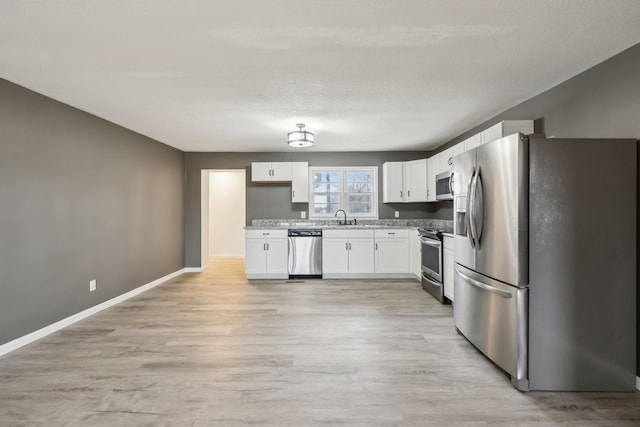 kitchen with appliances with stainless steel finishes, white cabinetry, sink, light hardwood / wood-style floors, and a textured ceiling