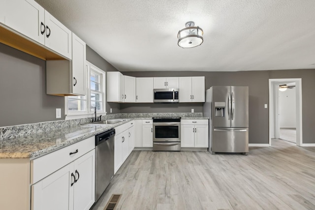 kitchen with stainless steel appliances, light stone countertops, sink, and white cabinets