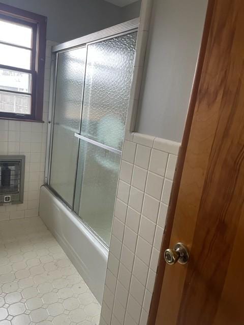 bathroom featuring bath / shower combo with glass door, heating unit, and tile walls