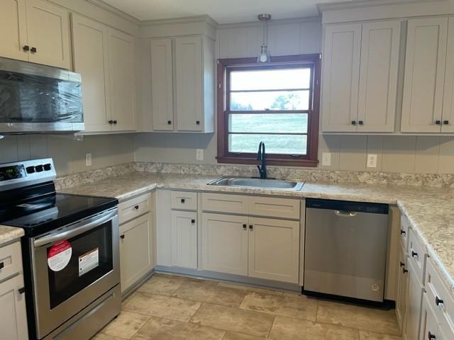 kitchen with appliances with stainless steel finishes, sink, white cabinets, and decorative light fixtures