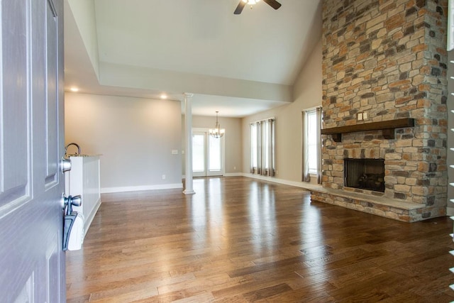 unfurnished living room with a stone fireplace, decorative columns, high vaulted ceiling, hardwood / wood-style flooring, and ceiling fan with notable chandelier