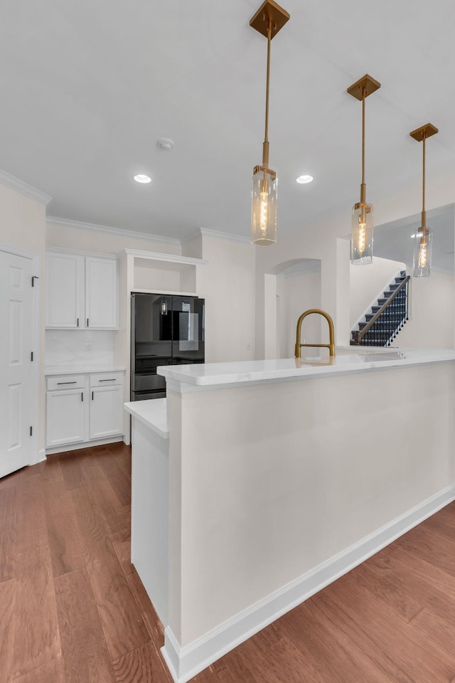 kitchen featuring black refrigerator, hardwood / wood-style floors, decorative light fixtures, white cabinetry, and crown molding