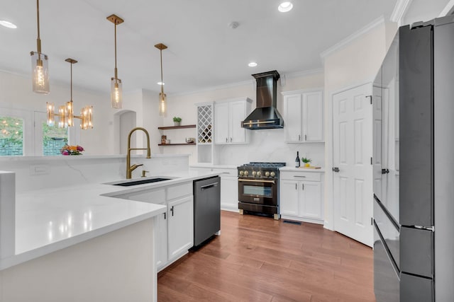 kitchen with sink, appliances with stainless steel finishes, pendant lighting, wall chimney range hood, and white cabinets