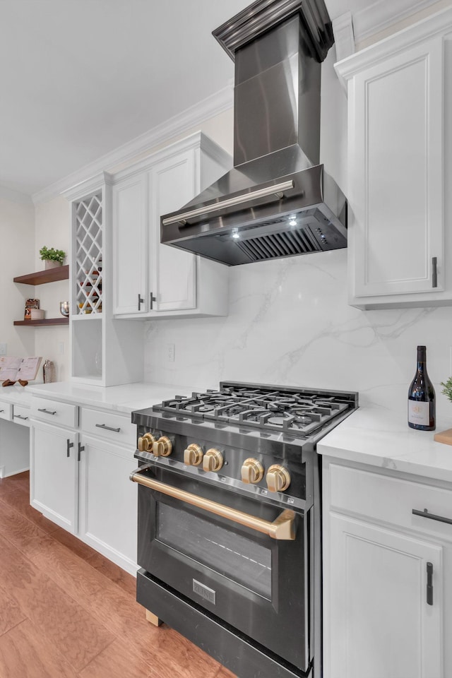 kitchen featuring range hood, high end stove, white cabinets, decorative backsplash, and light hardwood / wood-style flooring