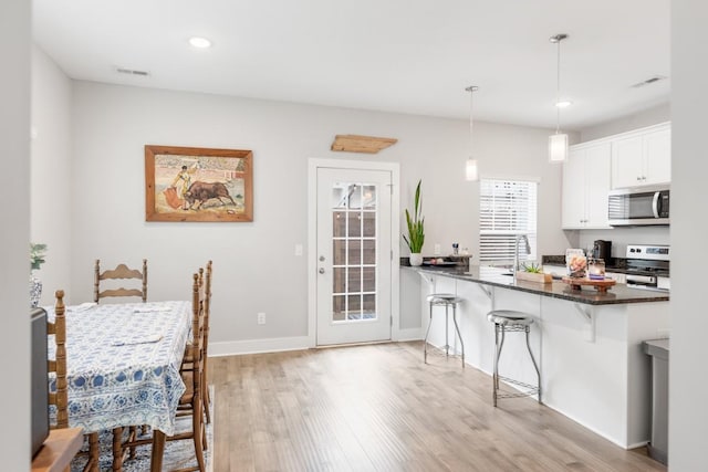 kitchen featuring appliances with stainless steel finishes, white cabinets, a kitchen bar, decorative light fixtures, and kitchen peninsula