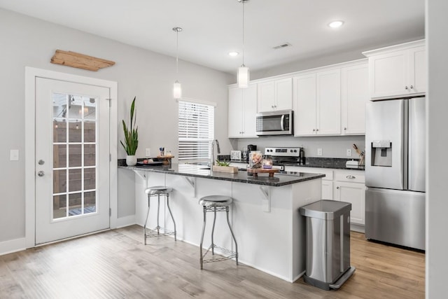 kitchen featuring pendant lighting, white cabinets, a kitchen bar, dark stone counters, and stainless steel appliances