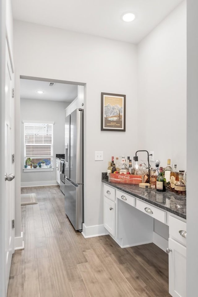 kitchen with white cabinets, stainless steel fridge, light wood-type flooring, and dark stone counters