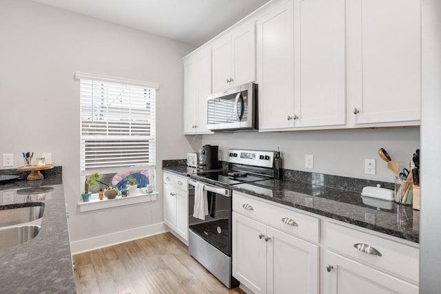 kitchen featuring white cabinetry, light hardwood / wood-style flooring, dark stone counters, and appliances with stainless steel finishes