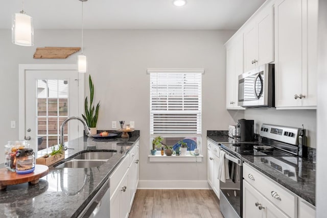 kitchen with sink, hanging light fixtures, stainless steel appliances, white cabinets, and dark stone counters