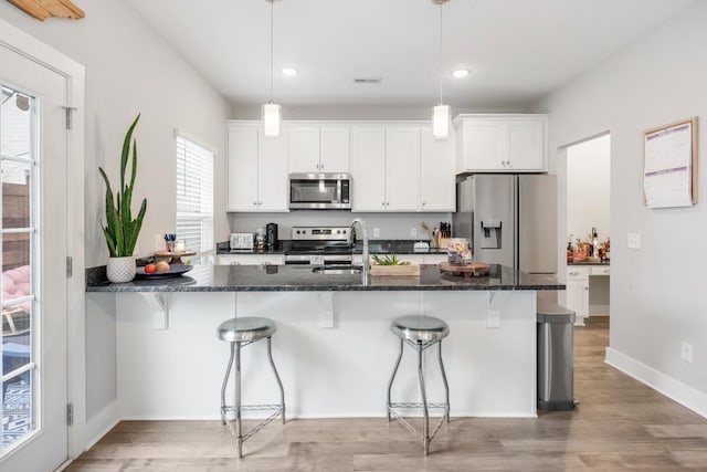 kitchen with hanging light fixtures, stainless steel appliances, a breakfast bar, and white cabinets