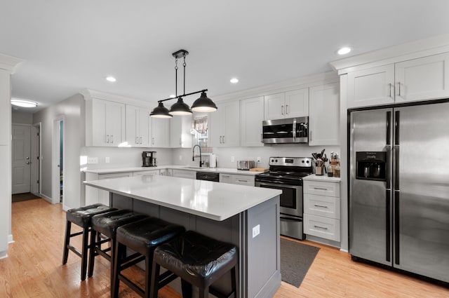 kitchen featuring a breakfast bar, decorative light fixtures, a kitchen island, stainless steel appliances, and white cabinets