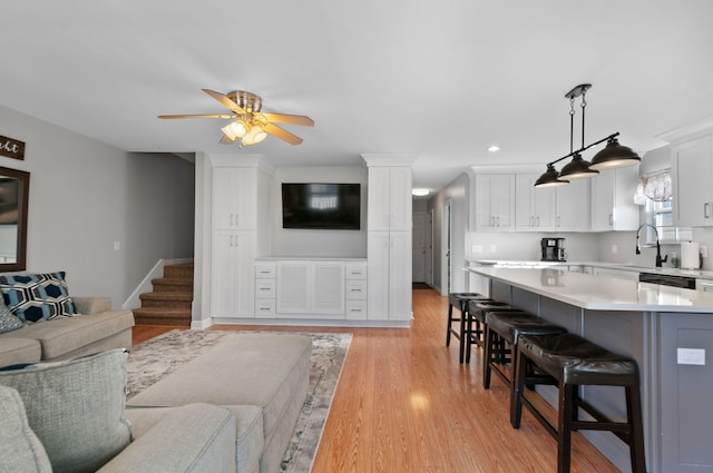 living room with ceiling fan, sink, and light wood-type flooring