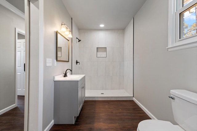 bathroom with a tile shower, vanity, wood-type flooring, and toilet