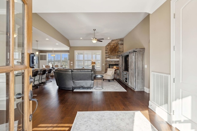 living room featuring a stone fireplace, dark wood-type flooring, ceiling fan, and vaulted ceiling