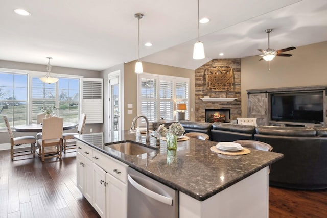 kitchen with sink, dark stone countertops, an island with sink, pendant lighting, and white cabinets