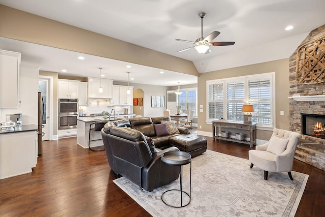 living room with lofted ceiling, a stone fireplace, dark hardwood / wood-style flooring, and ceiling fan