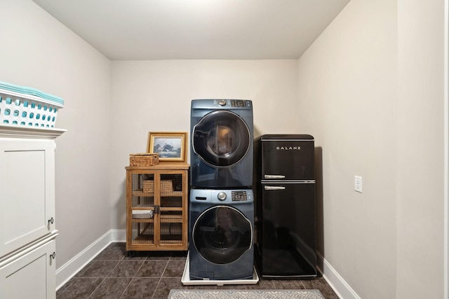 clothes washing area featuring dark tile patterned flooring, cabinets, and stacked washing maching and dryer