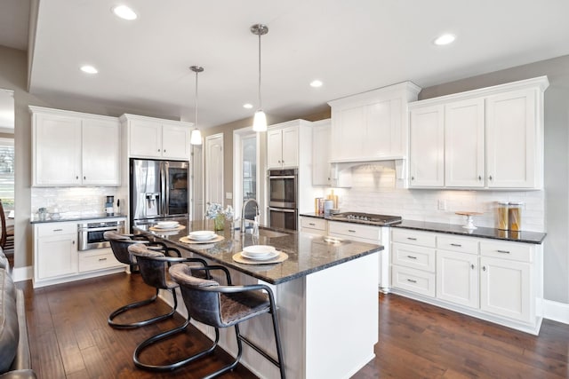 kitchen with pendant lighting, a breakfast bar area, appliances with stainless steel finishes, white cabinetry, and a center island with sink