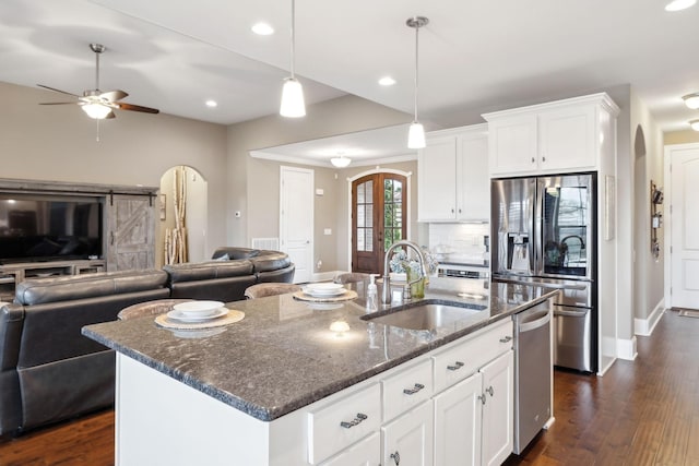 kitchen featuring sink, stainless steel appliances, white cabinets, a center island with sink, and dark stone counters