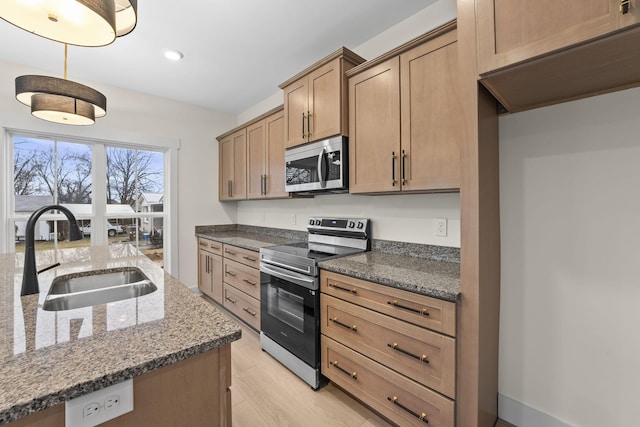 kitchen featuring sink, stainless steel appliances, light hardwood / wood-style floors, decorative light fixtures, and dark stone counters