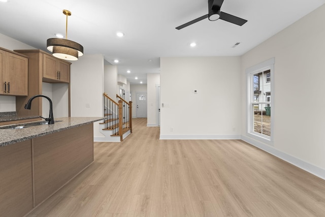 kitchen with light wood-type flooring, ceiling fan, sink, and dark stone countertops