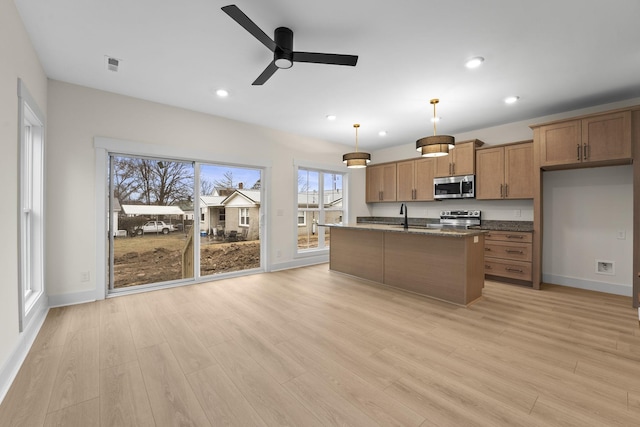 kitchen featuring stainless steel appliances, an island with sink, light hardwood / wood-style flooring, and decorative light fixtures