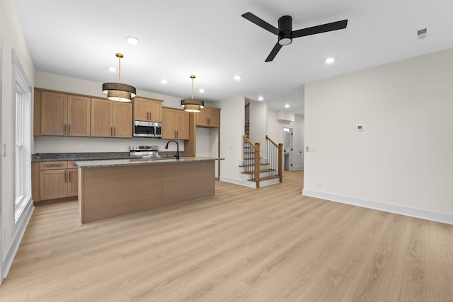 kitchen featuring sink, hanging light fixtures, light wood-type flooring, appliances with stainless steel finishes, and an island with sink