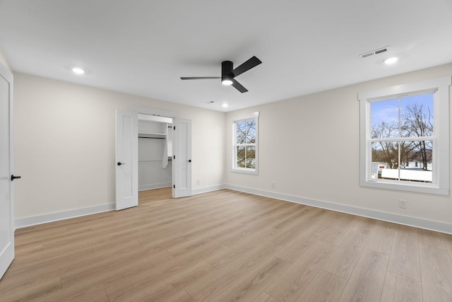 unfurnished bedroom with ceiling fan, a walk in closet, multiple windows, and light wood-type flooring